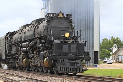 Image of a giant steam locomotive. World's largest. It is standing on tracks in aninustrial rail yard.