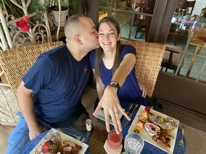 Couple at Breakfast, he is giving her a kiss on the cheek as she holds her engagement ring up to the camera!