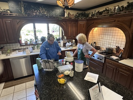  Chef Lisa Jassund teaching an Acclaimed Cooking Class on the subject of Italian cooking.
Shown in the professional kitchen at Annville Inn.
Twowomen in large room, with a giant picture window across back of kitchen with view of mountains.
