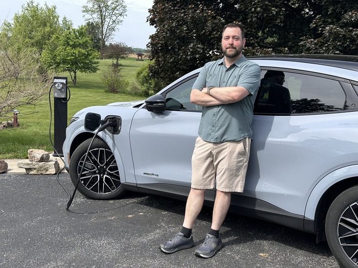 A man standing beside an EV Charging Point, charging his vehicle.