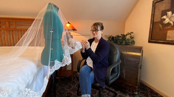 Mother sewing her daughter's bridal veil in Annville Inn's Secret Guest Room. Light comes through door window, highlighting her.