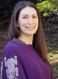 A head shot photo of Heather Simpson wearing a purple shirt with off white First Nations frogs on the arm