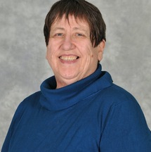 A head shot of Jeannie Mills wearing a sweater and smiling toward the camera.