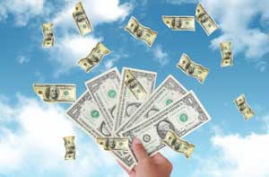 Hand holds up money against a blue sky with white clouds