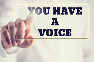 IMAGE: Someone points to black bold block letters on a glass board which spell out You Have A Voice